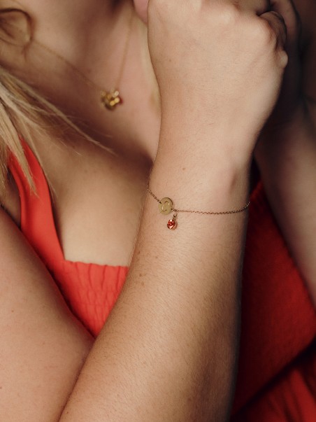 Foto de un brazo luciendo una pulsera dorada con la letra C y una piedra circonita de color naranja de la marca AmaloA.